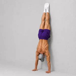Kal holding a chest-to-wall handstand with straight arms and toes lightly touching the wall
